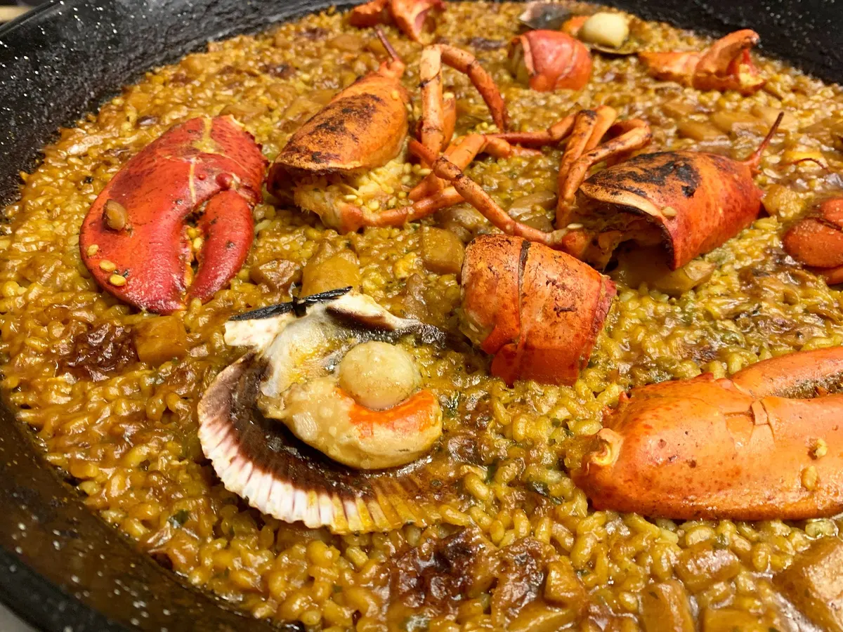 Paella de arroz con bogavante troceado y vieira, vista de cerca en la paellera de Cuina de Sabors
