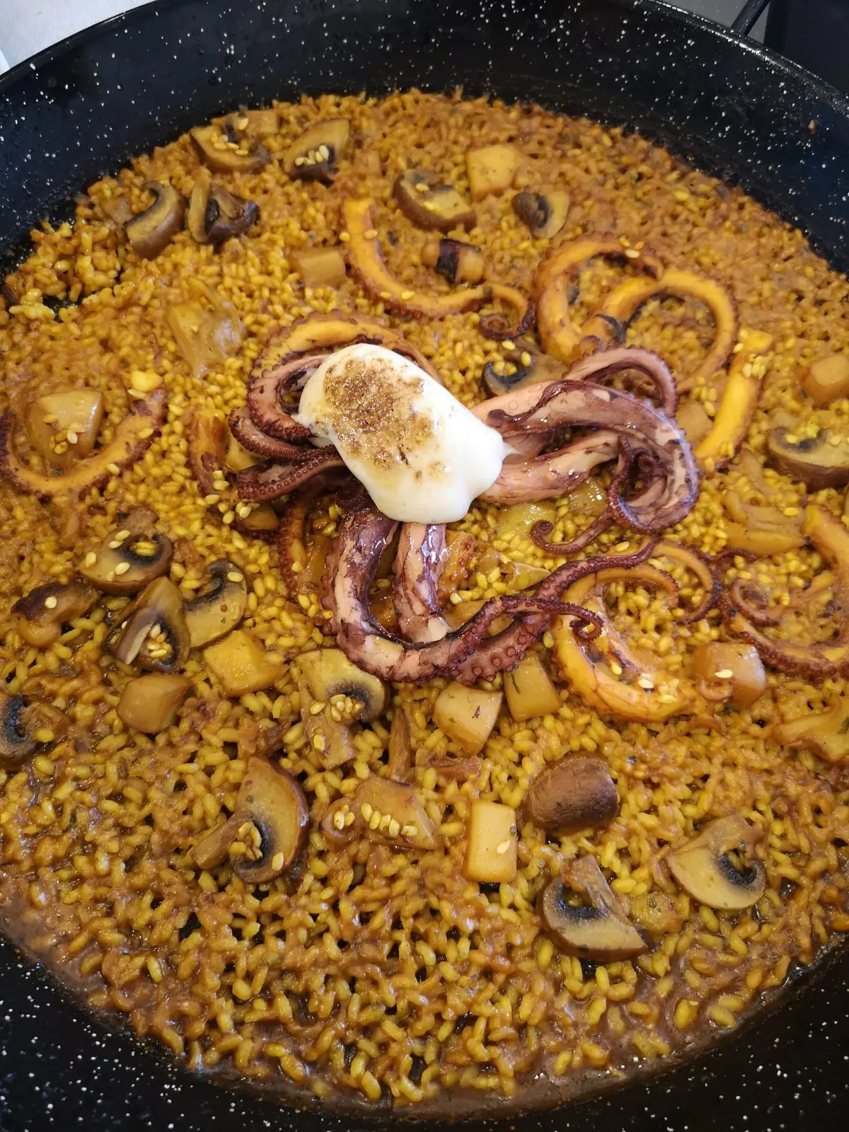 Paella de arroz con pulpo, champiñones y anillas de calamar, con una cucharada de alioli en el centro