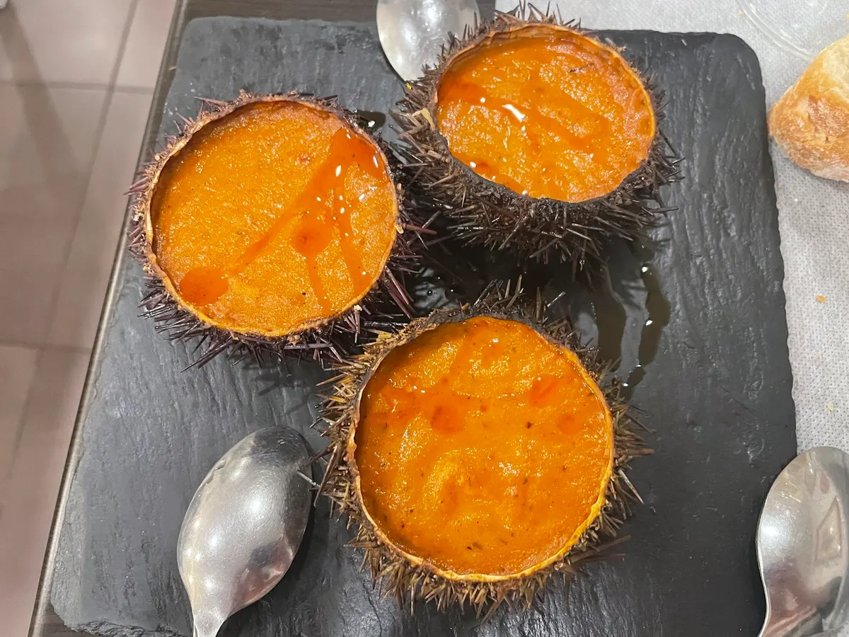Tres erizos de mar gratinados sobre una pizarra negra, con cucharillas
