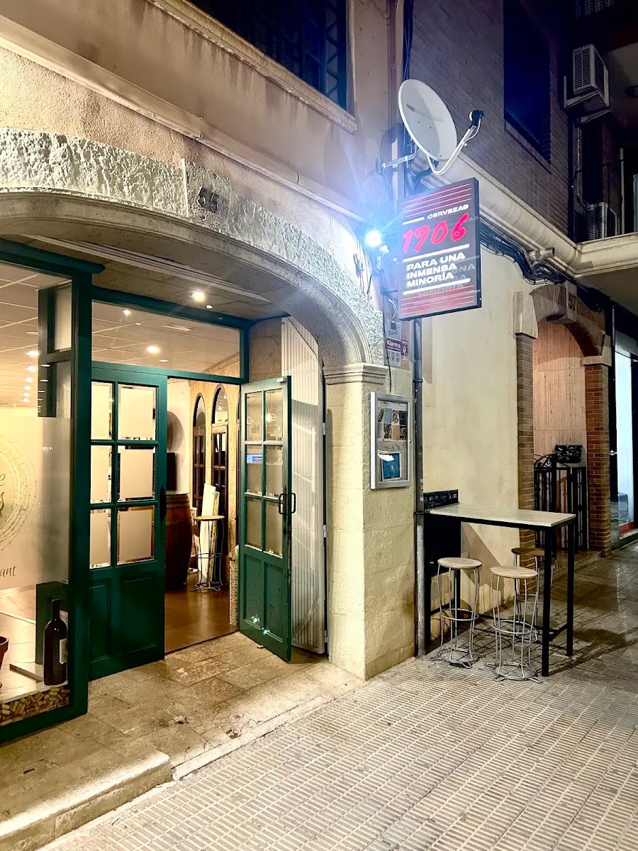 Entrada de Cuina de Sabors de noche: arco de piedra con el número 55 y puertas acristaladas verdes abiertas