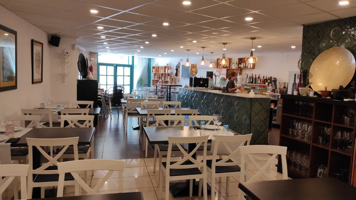 Comedor de Cuina de Sabors con sillas blancas de aspa, mesas oscuras y la barra de azulejo verde al fondo