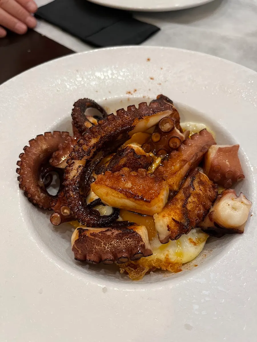 Pulpo a la plancha sobre huevo frito en un plato hondo blanco